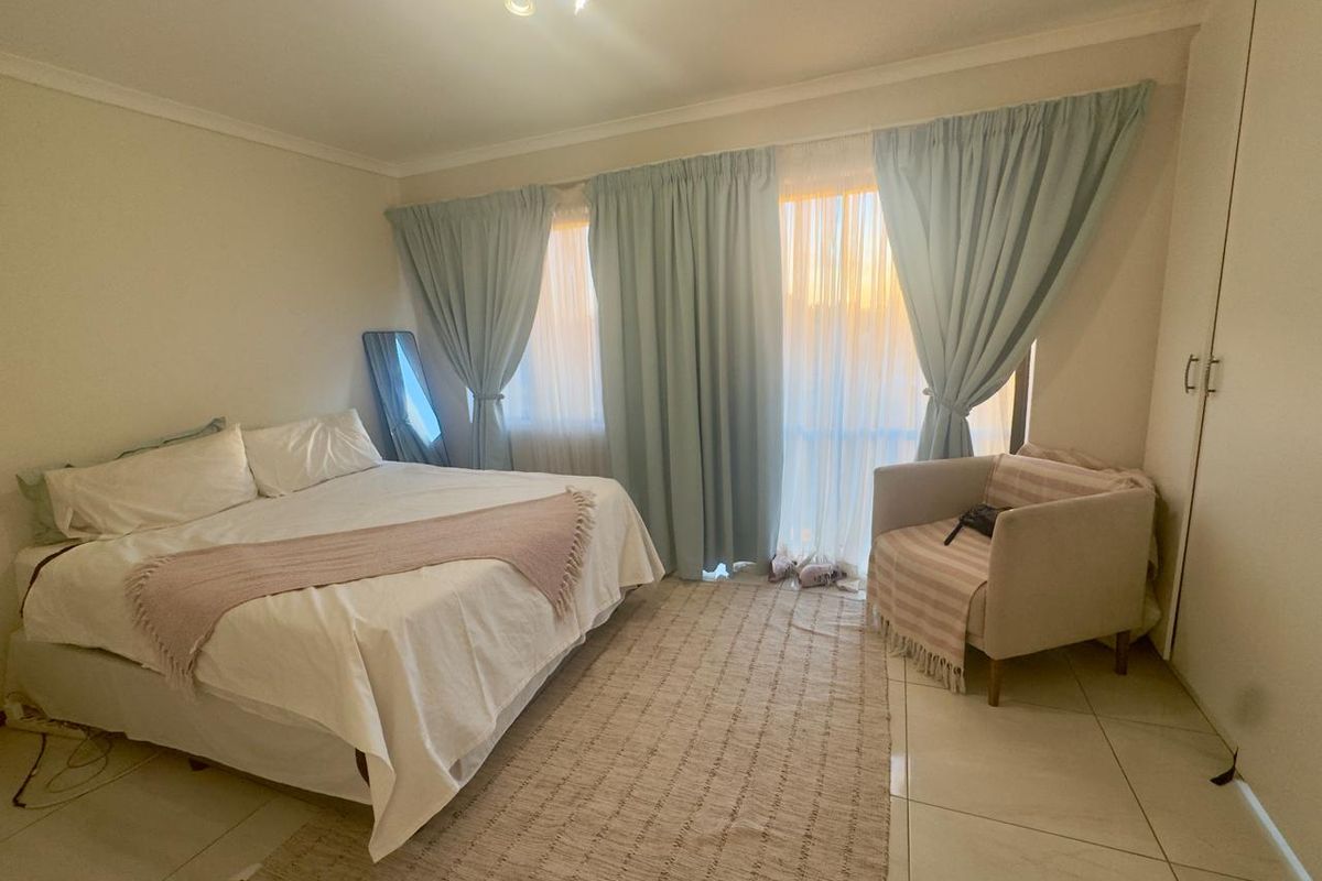 A well-lit bedroom featuring neutral tiled flooring, a built-in wardrobe, and large windows with curtains, providing a comfortable and functional living space.
