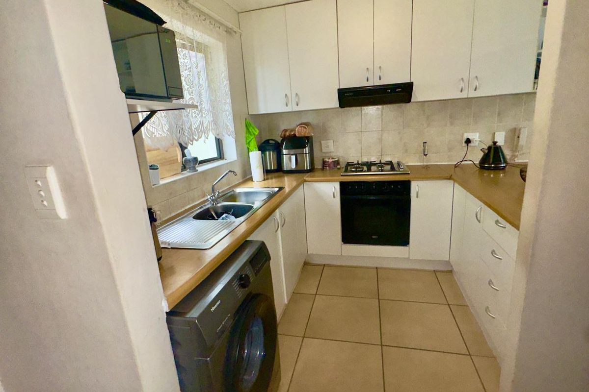 Compact kitchen featuring white cabinetry, laminate countertops, built-in oven, gas hob, extractor fan, and tiled flooring with integrated laundry plumbing.