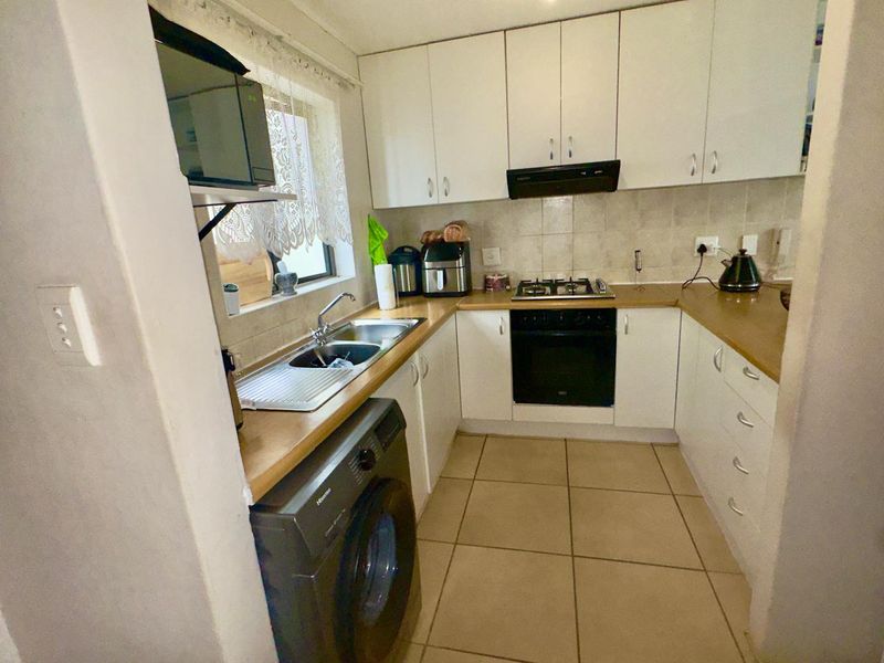 Compact kitchen featuring white cabinetry, laminate countertops, built-in oven, gas hob, extractor fan, and tiled flooring with integrated laundry plumbing.
