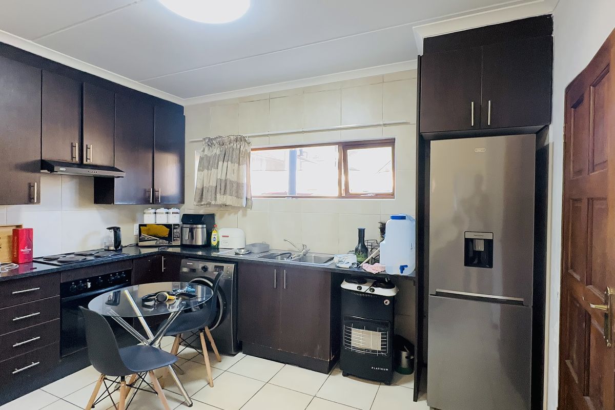 A functional kitchen featuring dark wood cabinetry, built-in oven with hob, extractor fan, and tiled finishes throughout.