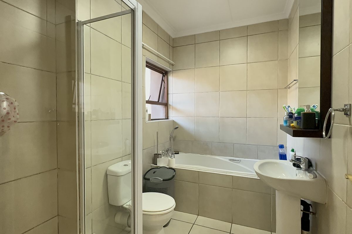 A functional bathroom featuring a shower enclosure, bathtub, pedestal basin, and toilet with neutral wall and floor tiling.