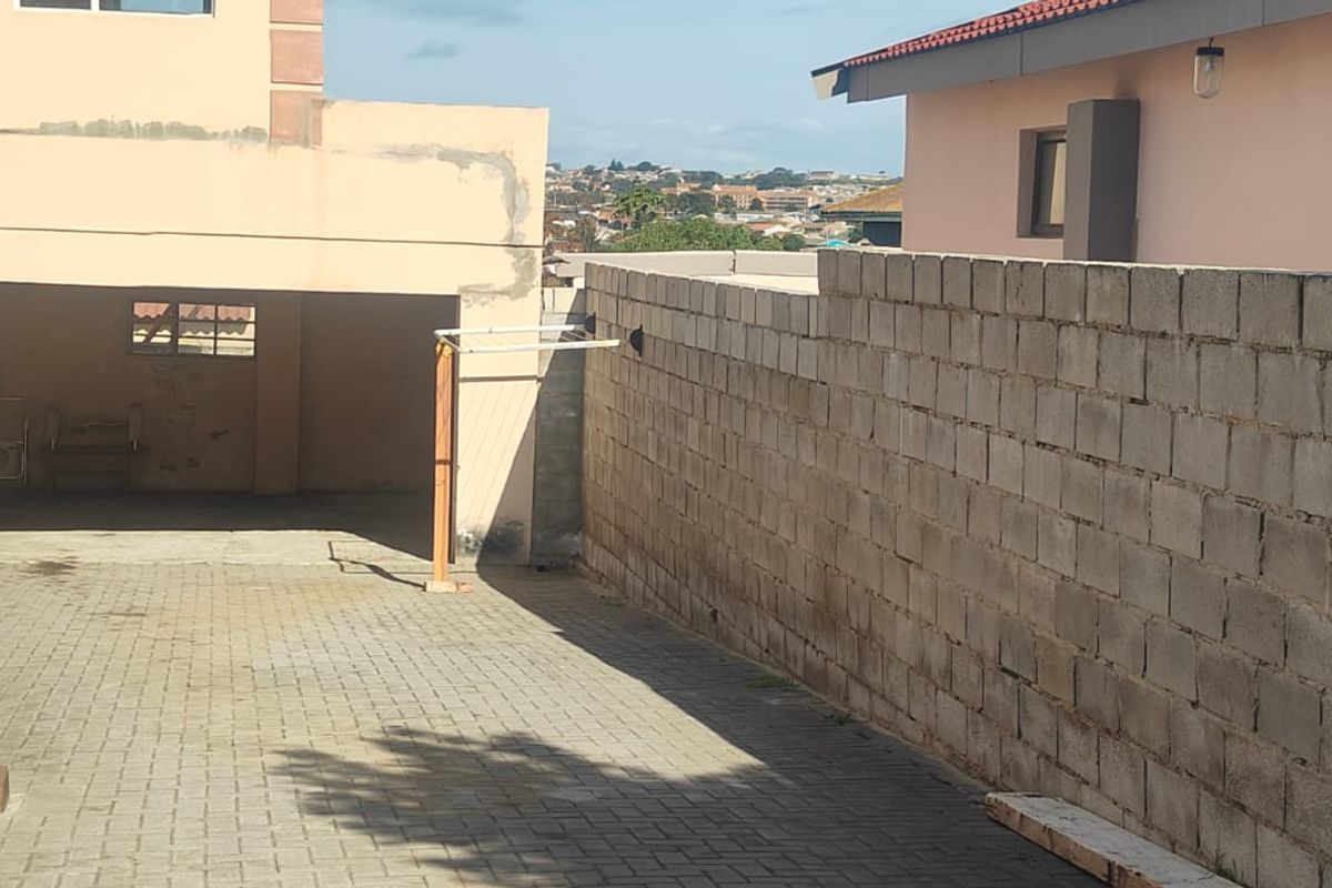 Rear exterior area featuring a paved driveway, a covered carport, and an unfinished concrete block boundary wall.