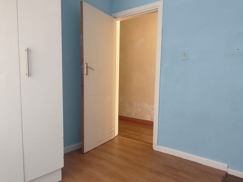 A bedroom featuring laminate flooring and built-in cupboards, showing signs of wear on the walls and door requiring cosmetic attention.
