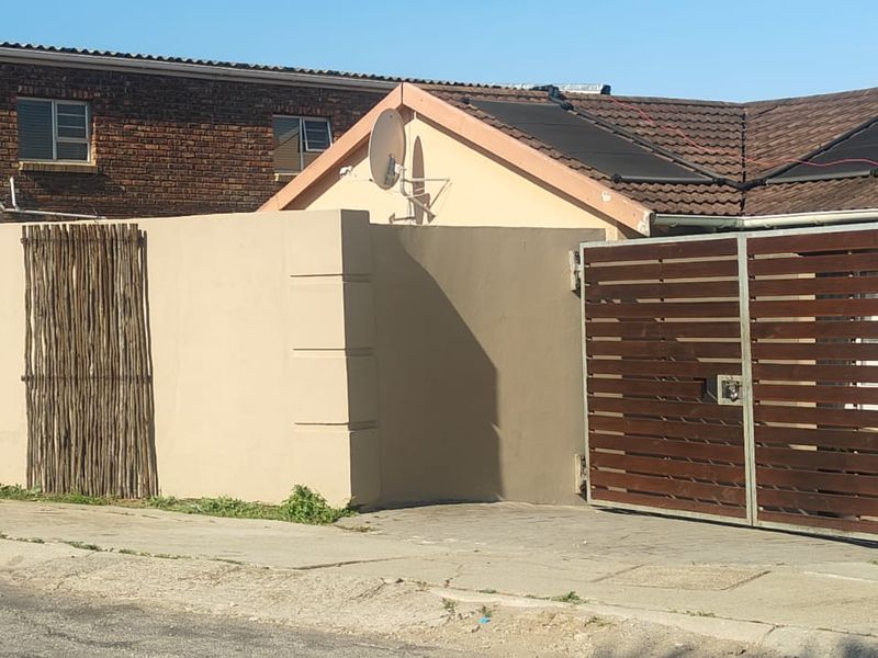 Front exterior view of the property featuring a solid boundary wall, slatted timber gate, and roof-mounted solar water heating panels.