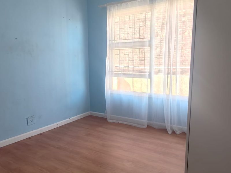 A vacant bedroom featuring laminate flooring, blue painted walls, and a window fitted with security bars.