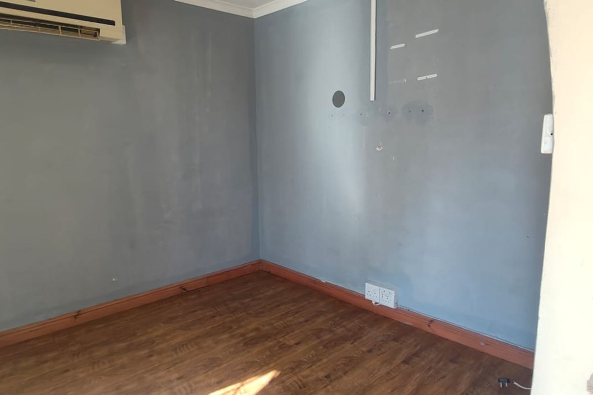 An empty living room featuring laminate flooring, a wall-mounted air conditioning unit, and visible wall surface imperfections requiring cosmetic attention.