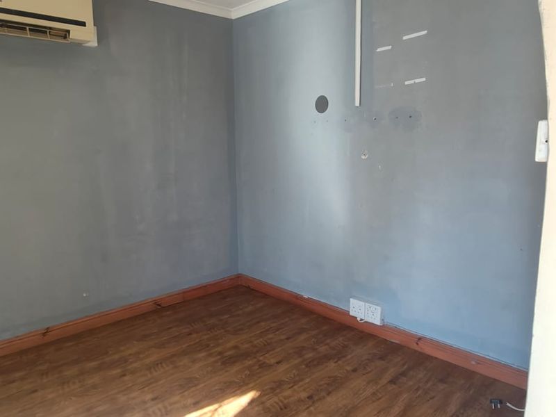 An empty living room featuring laminate flooring, a wall-mounted air conditioning unit, and visible wall surface imperfections requiring cosmetic attention.