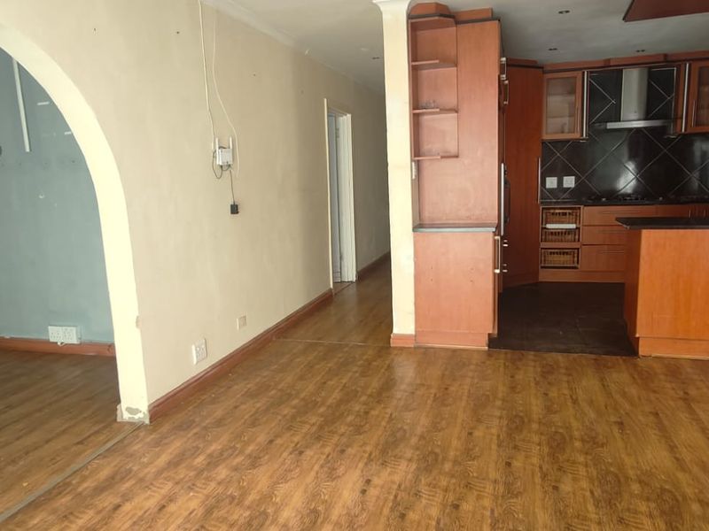 Open plan living area featuring laminate flooring, an arched transition, and a dated wooden kitchen with built-in cabinetry and gas hob.