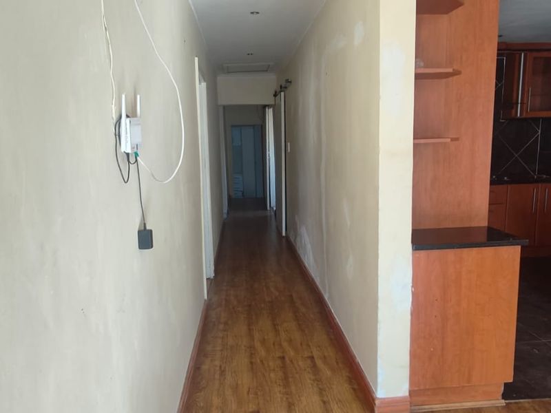 A long hallway with laminate flooring leading towards a kitchen area featuring wooden cabinetry and dark countertops.
