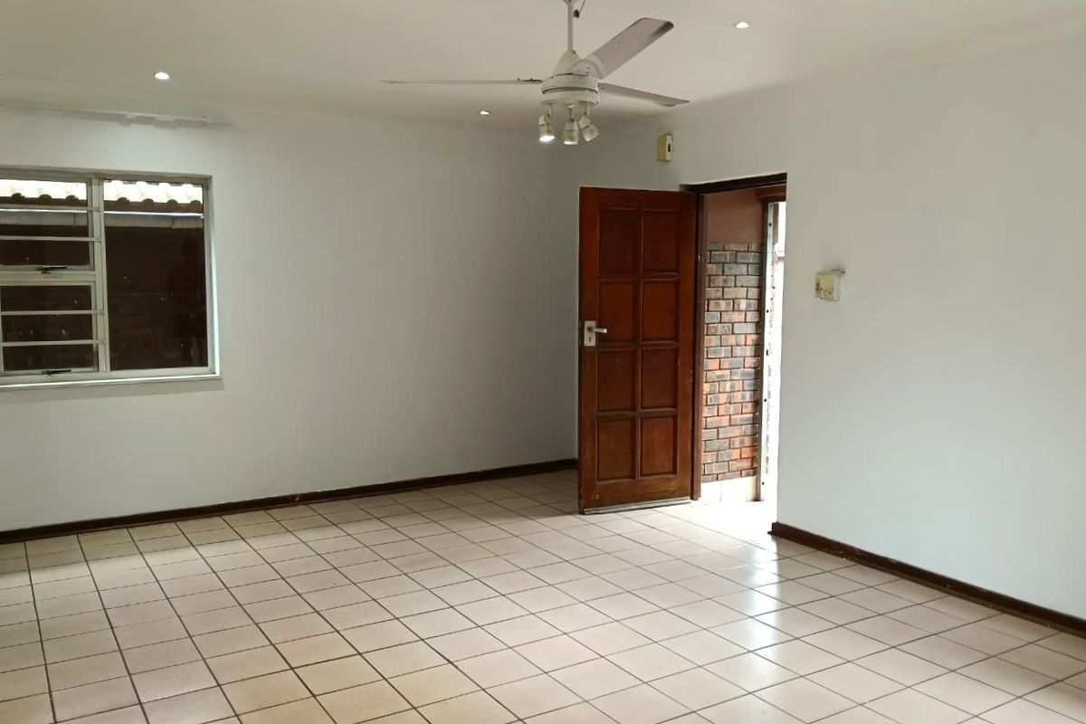An empty living room featuring neutral tiled flooring, a ceiling fan, recessed lighting, and a timber entrance door leading to an exterior brick walkway.