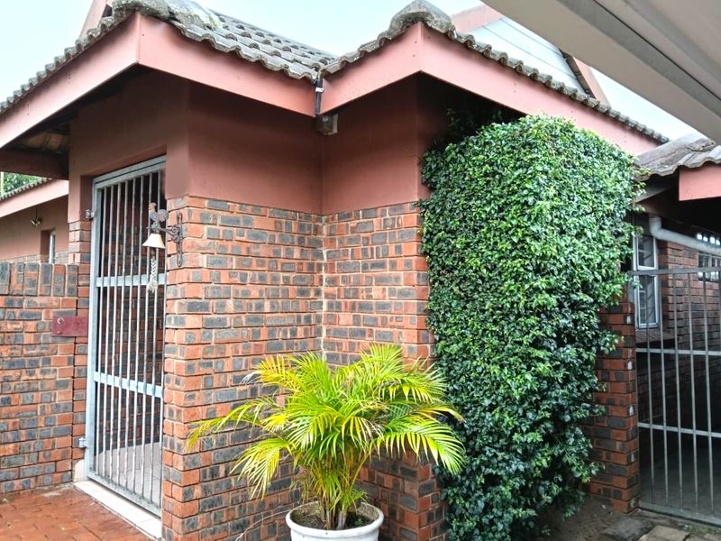 Exterior view of a townhouse featuring face brick walls, a tiled roof, and secure metal gates at the entrance.
