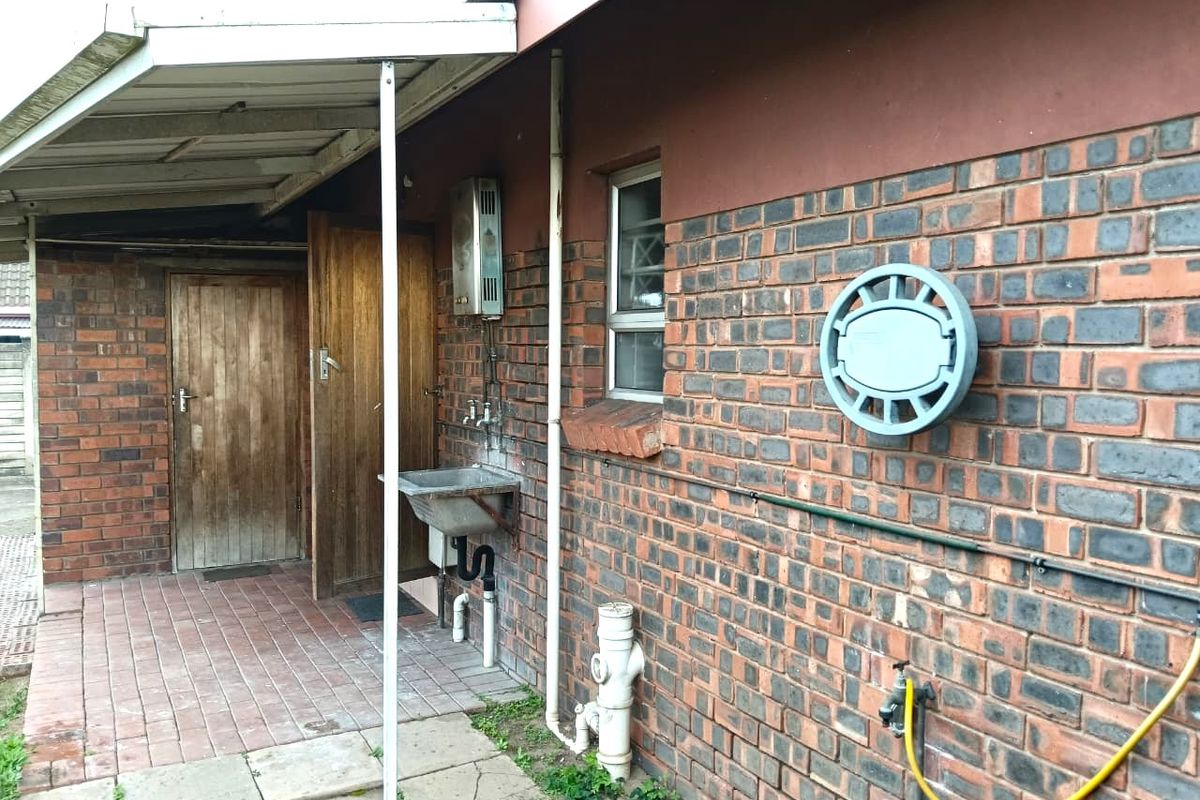 Rear exterior view of the townhouse featuring a brick facade, utility sink, gas geyser, and a covered patio area.