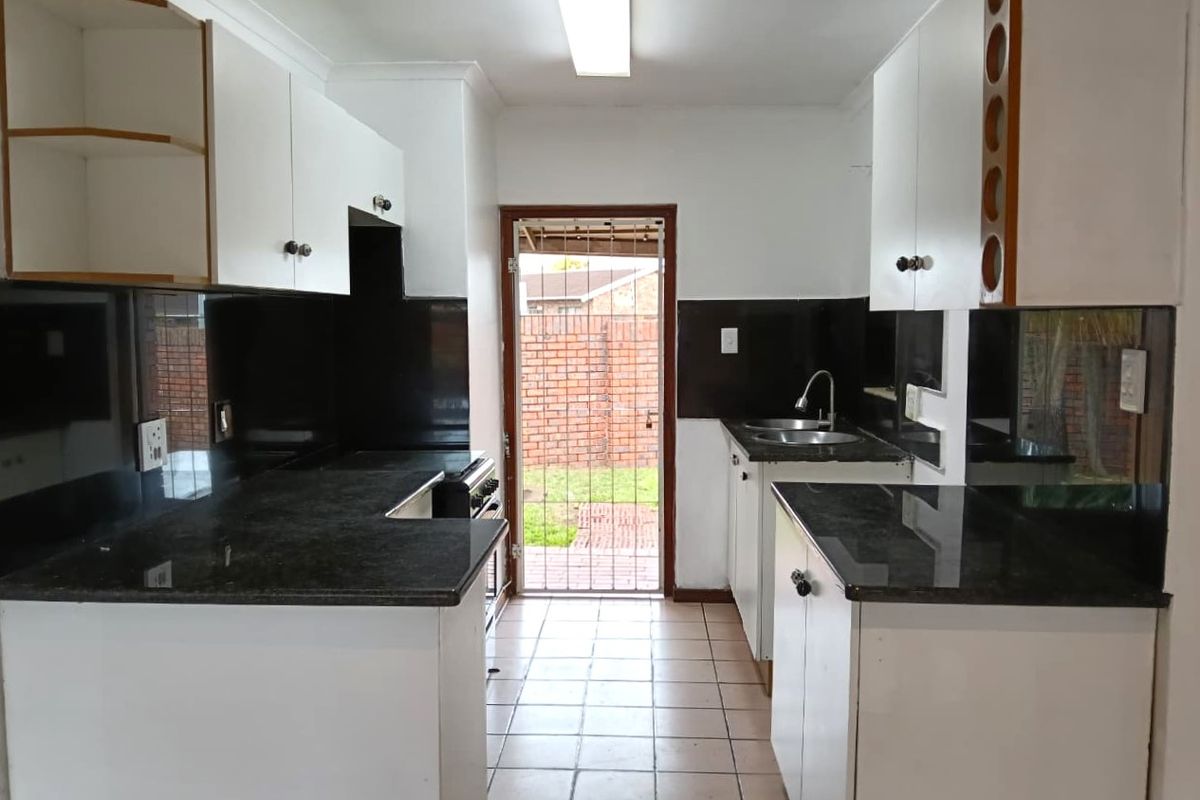 A functional kitchen featuring white cabinetry, dark granite countertops, tiled splashbacks, and direct access to the rear exterior through a security gate.