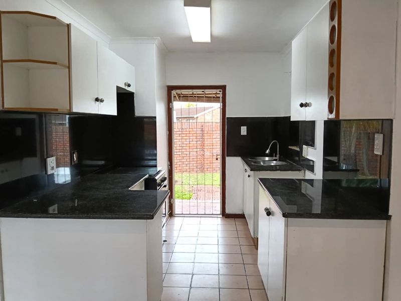 A functional kitchen featuring white cabinetry, dark granite countertops, tiled splashbacks, and direct access to the rear exterior through a security gate.