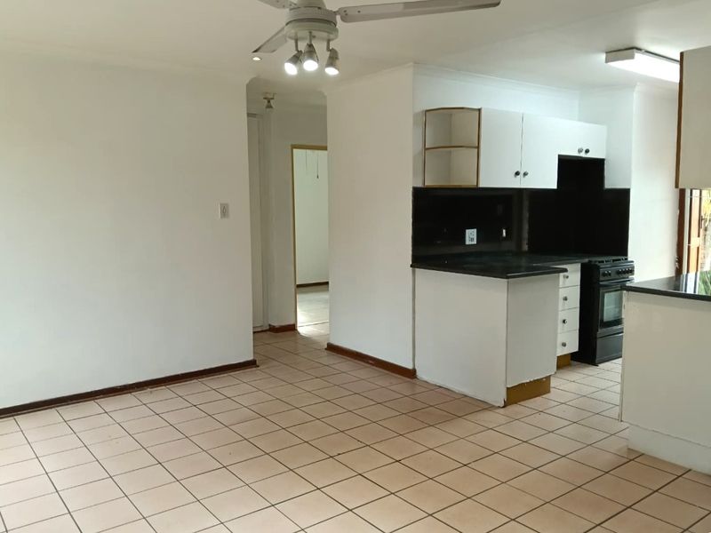 Open plan living and kitchen area featuring tiled flooring, ceiling fan, and basic built-in cabinetry with a freestanding oven.