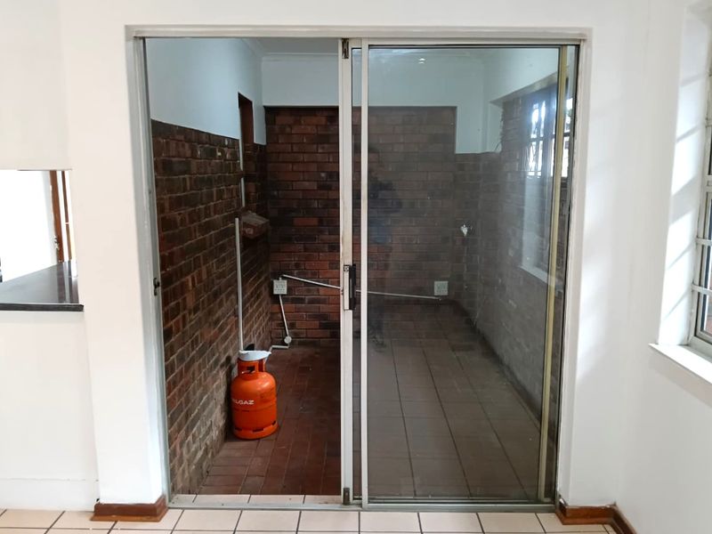 A functional scullery or utility area featuring exposed brick walls, tiled flooring, and a sliding glass door entrance.