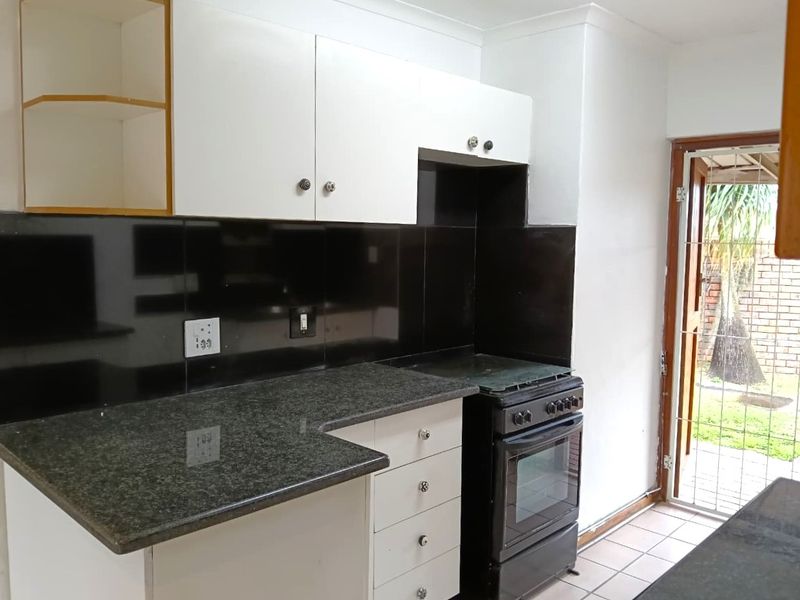 A functional kitchen featuring granite countertops, black splashback, and white cabinetry, with direct access to the rear garden area.