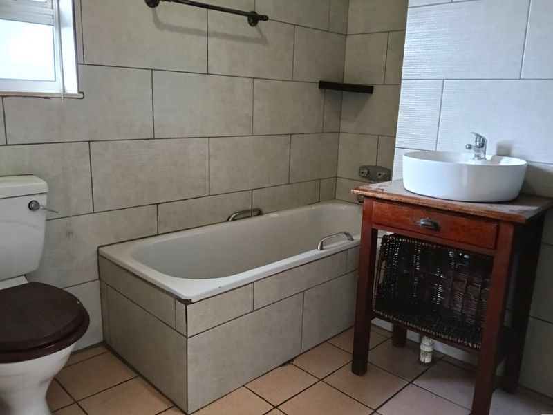 A functional bathroom featuring a bathtub, toilet, and a vessel sink vanity with neutral wall and floor tiling.
