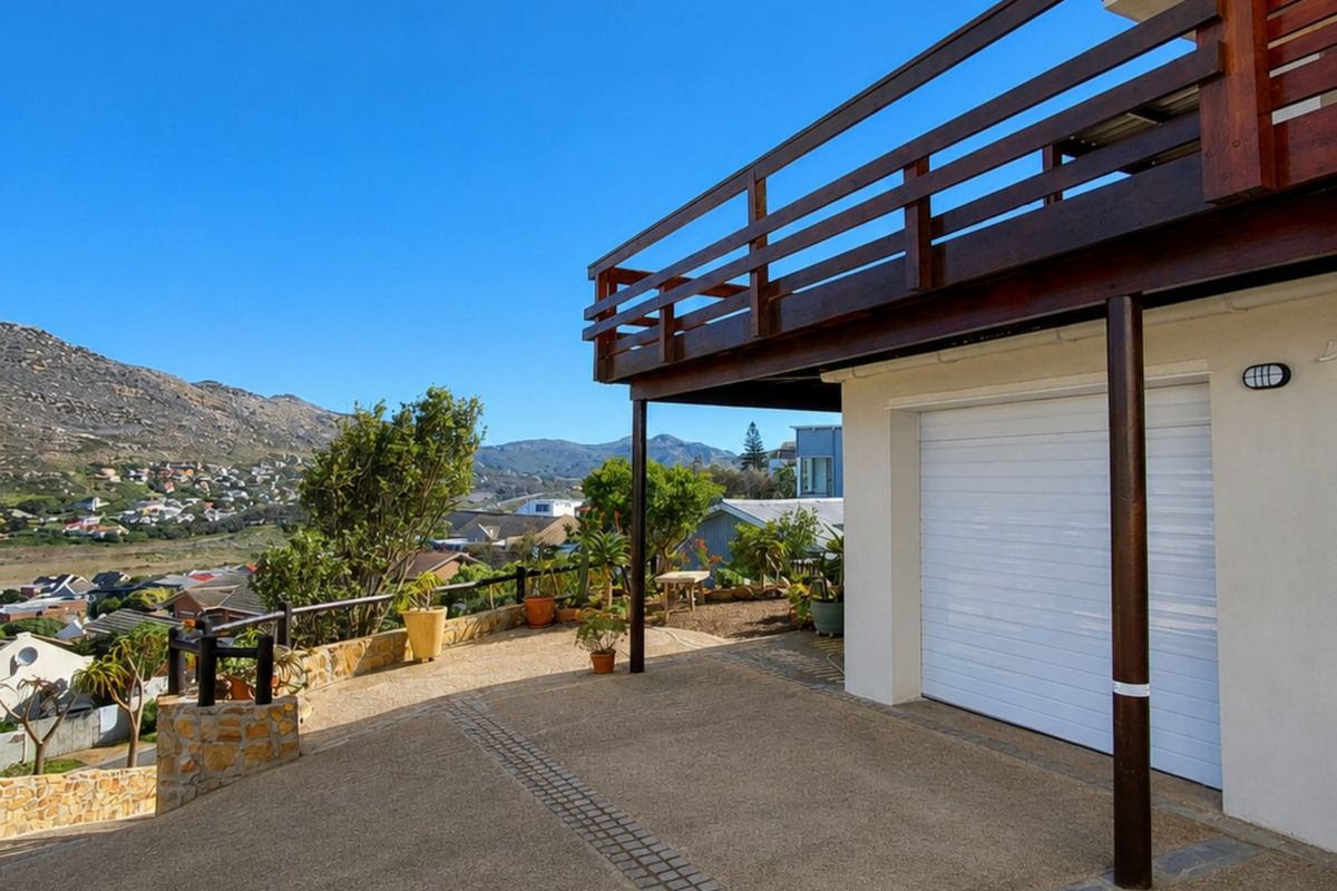 Rear exterior view featuring a paved driveway, garage access, and a wooden balcony overlooking the surrounding landscape.