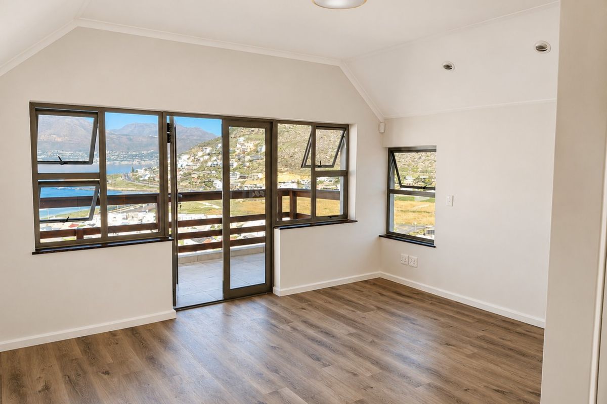 A bright, empty bedroom featuring vaulted ceilings, modern laminate flooring, and large windows with direct access to a balcony offering scenic coastal views.