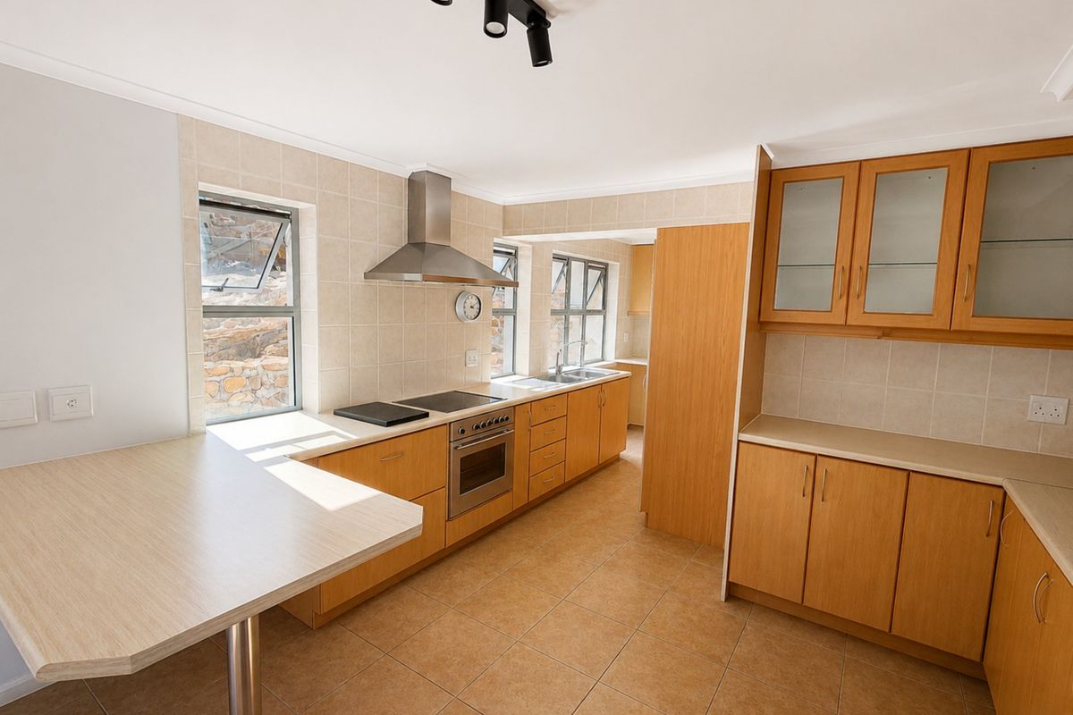 A functional kitchen featuring light wood cabinetry, tiled splashbacks, built-in oven with extractor fan, and tiled flooring, offering a clean and practical workspace.