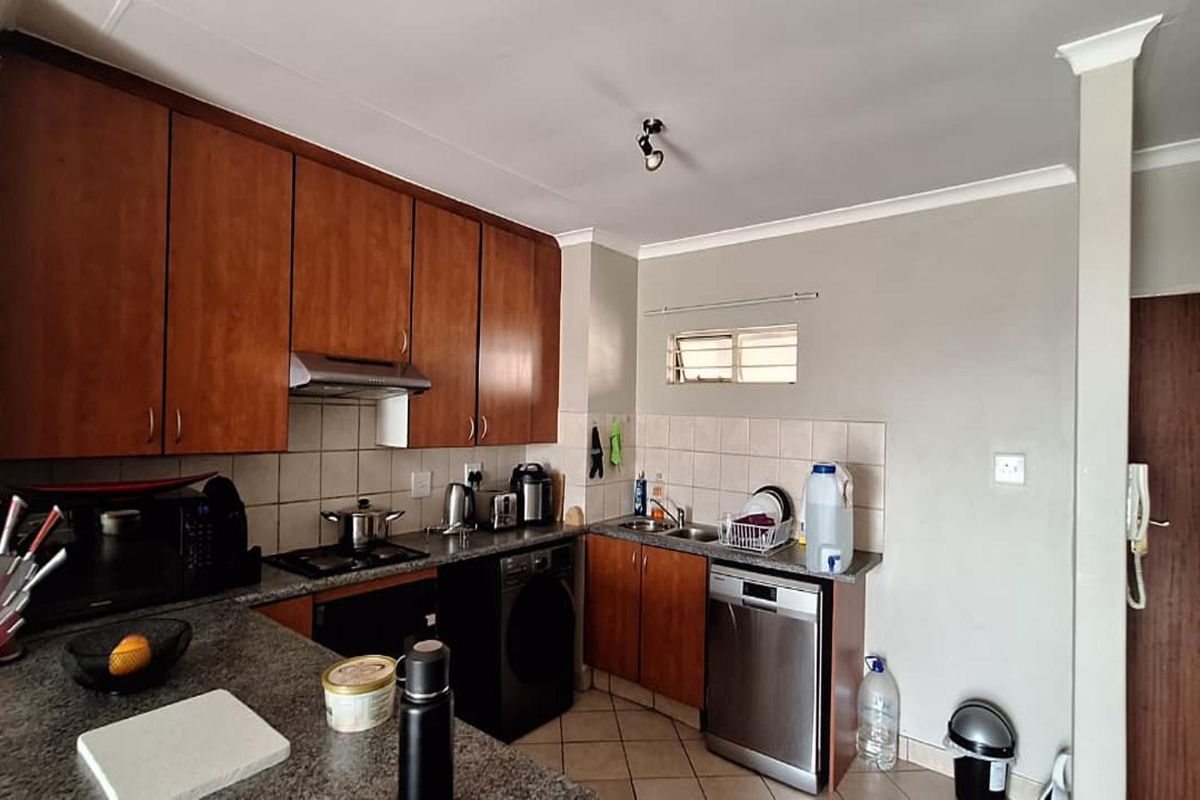 A functional kitchen featuring wooden cabinetry, laminate countertops, a built-in hob with extractor fan, and tiled flooring with a tiled backsplash.