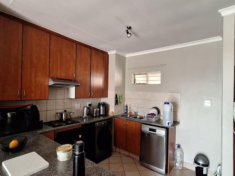 A functional kitchen featuring wooden cabinetry, laminate countertops, a built-in hob with extractor fan, and tiled flooring with a tiled backsplash.