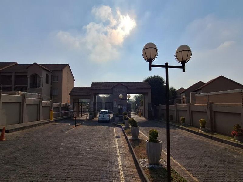 The entrance to the apartment complex features a secure gated access point, paved driveway, and perimeter walling with electric fencing.