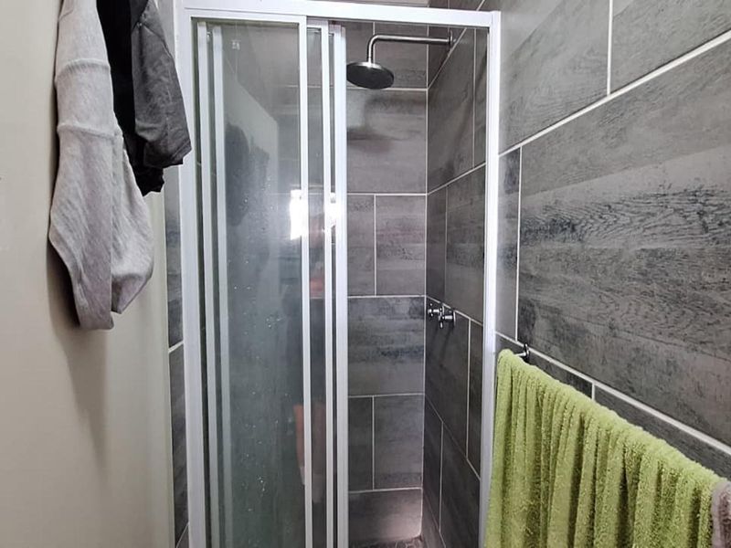 A modern bathroom shower featuring grey wood-look wall tiles and a glass-enclosed shower unit with a fixed shower head.