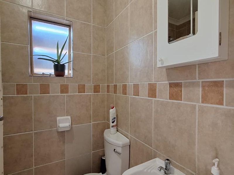 A compact bathroom featuring neutral ceramic wall tiles, a wall-mounted medicine cabinet, a standard toilet, and a small basin.