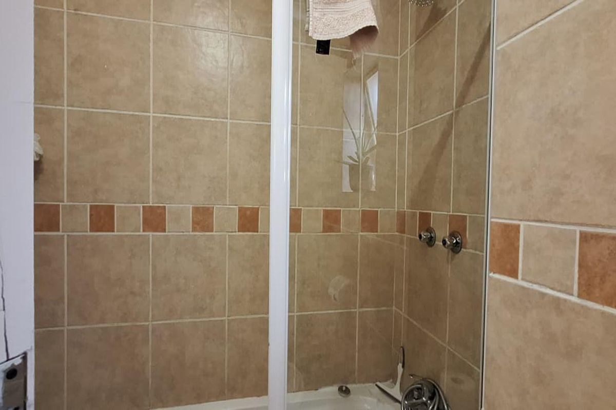 A shower enclosure featuring beige wall tiles with a decorative border, showing signs of wear on the adjacent door frame.
