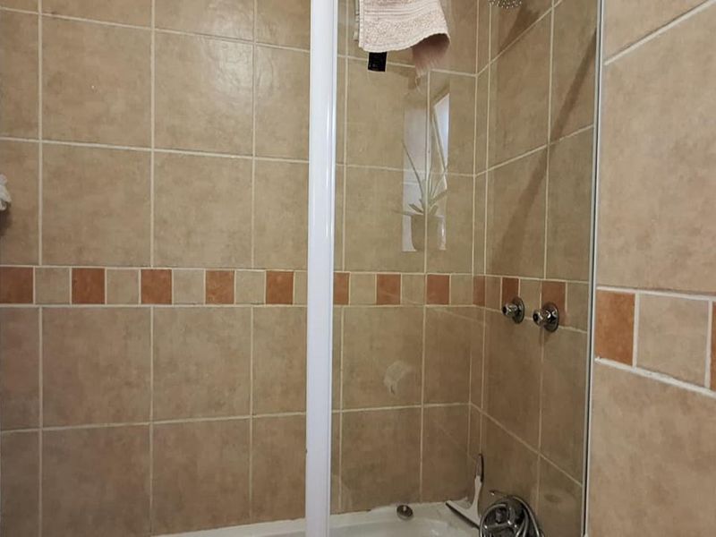 A shower enclosure featuring beige wall tiles with a decorative border, showing signs of wear on the adjacent door frame.