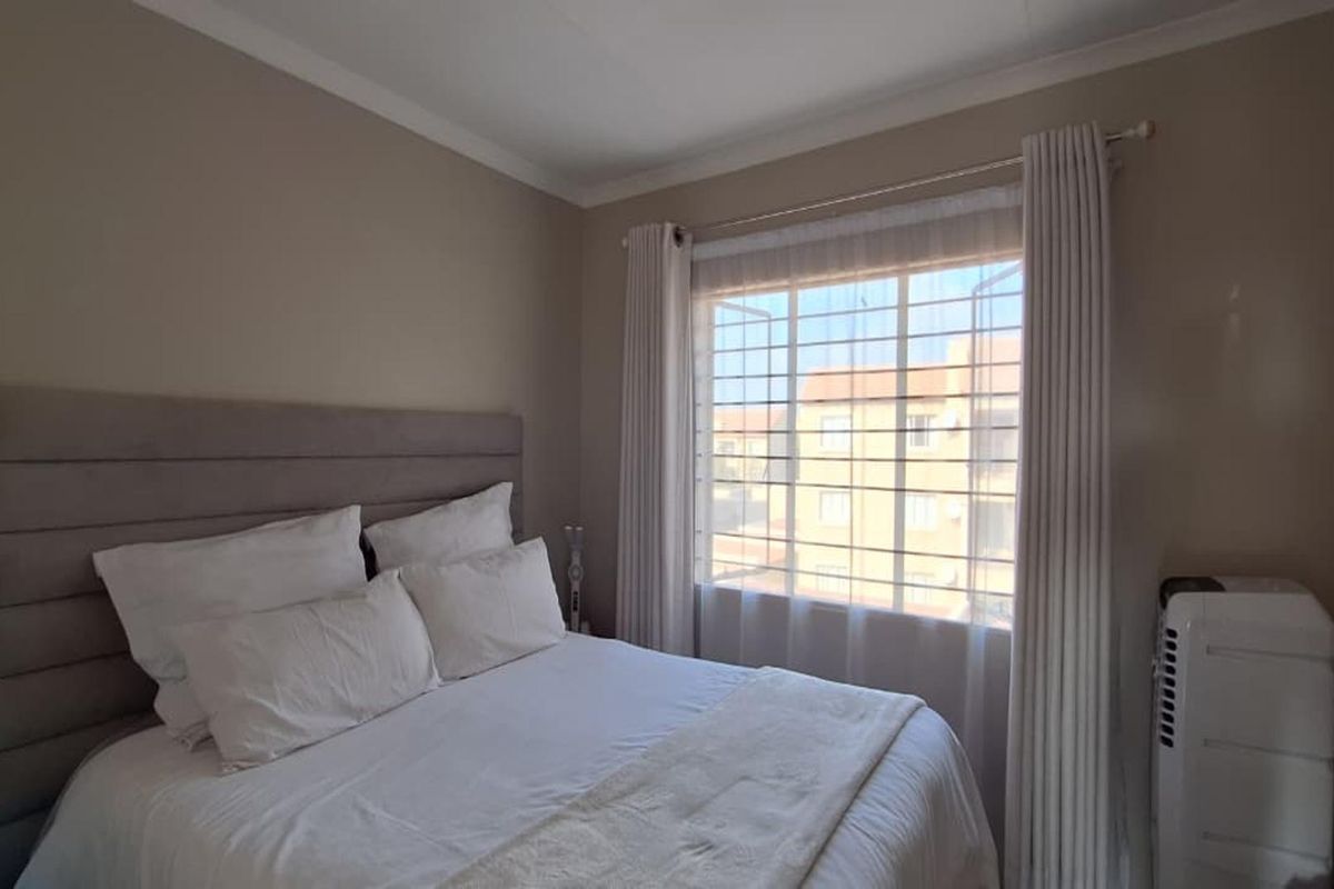 A well-maintained bedroom featuring neutral wall tones, a window with security bars, and fitted curtain rails.