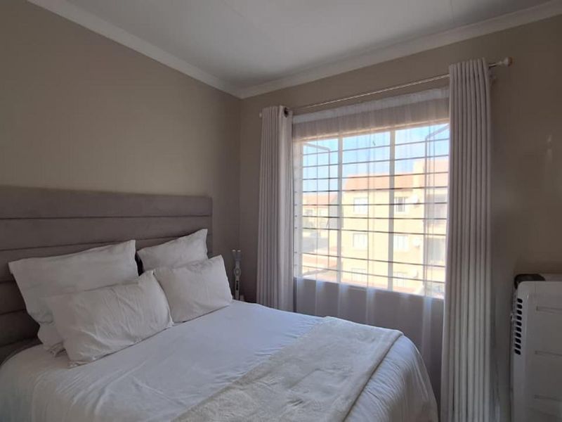 A well-maintained bedroom featuring neutral wall tones, a window with security bars, and fitted curtain rails.