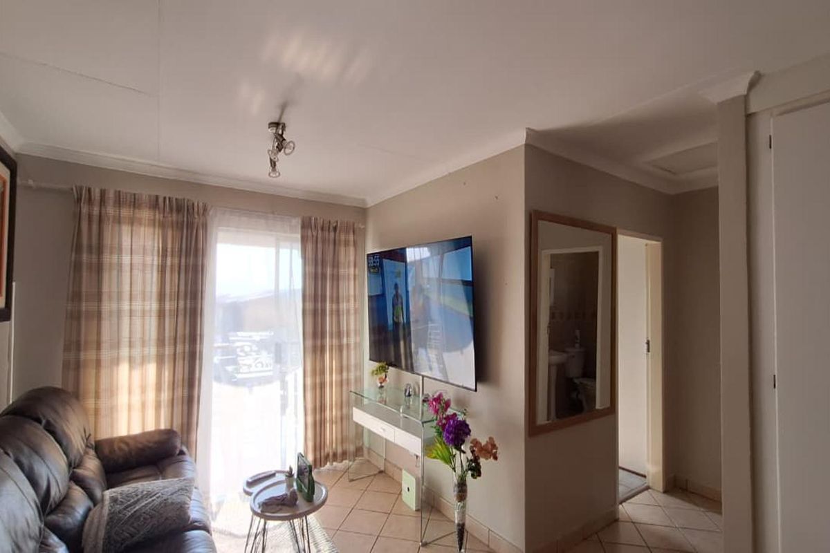 A living room featuring tiled flooring, coved ceilings, and a sliding glass door providing access to the exterior.