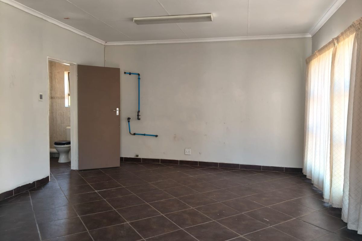 An empty bedroom featuring tiled flooring, coved ceilings, and exposed surface-mounted plumbing pipes on the wall, leading to an en-suite bathroom.