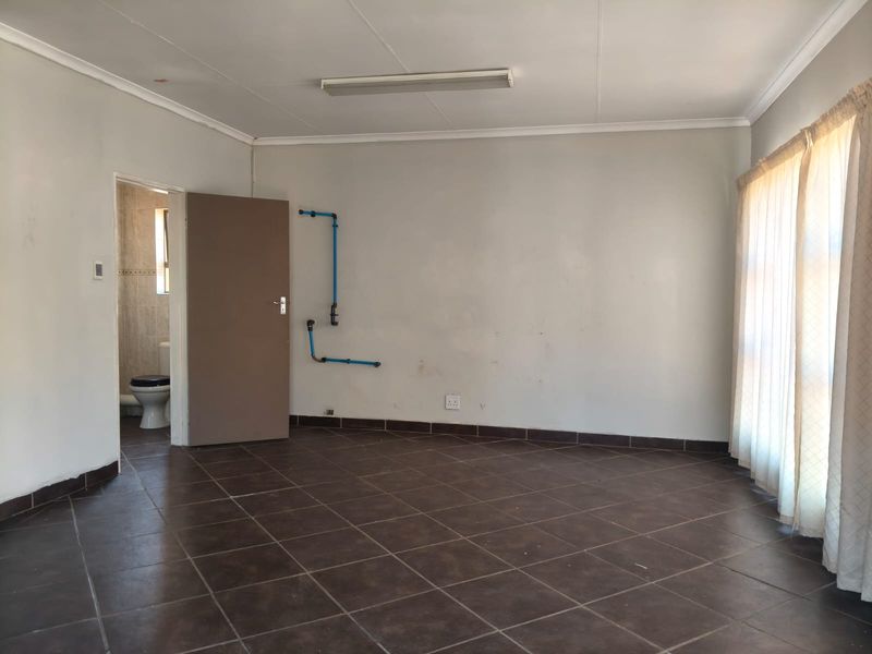 An empty bedroom featuring tiled flooring, coved ceilings, and exposed surface-mounted plumbing pipes on the wall, leading to an en-suite bathroom.