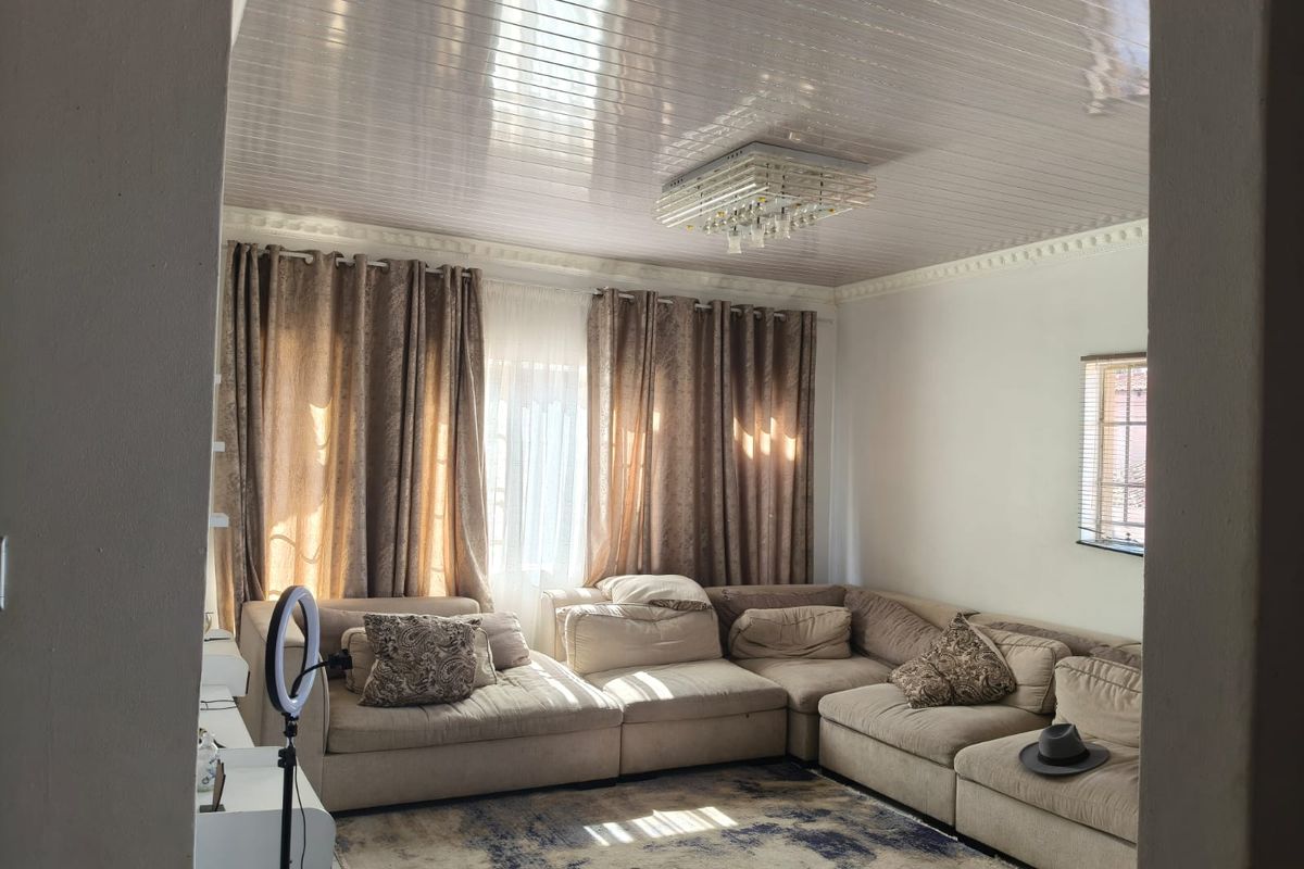 A comfortable living room featuring a glossy panelled ceiling, decorative cornice, and a central crystal light fixture, providing a bright and inviting space.