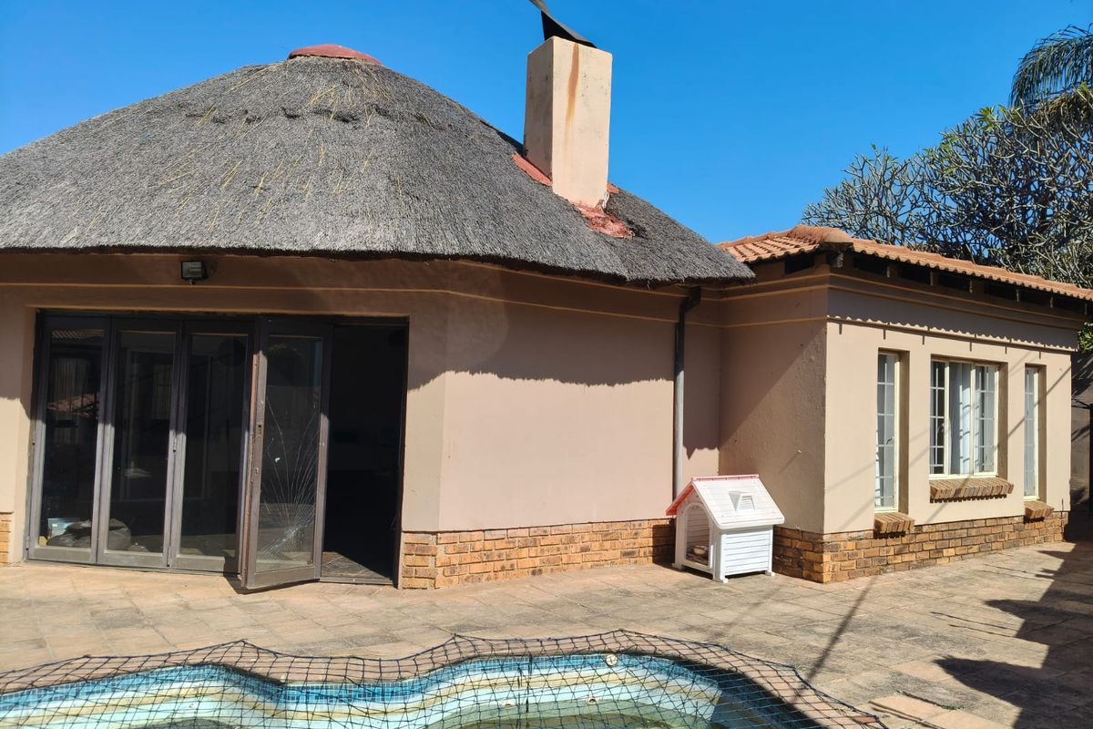 Rear exterior view featuring a thatched roof house, paved patio area, and a swimming pool with safety net.