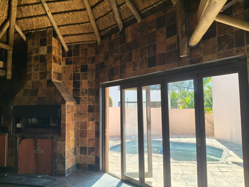 Covered outdoor entertainment area featuring a built-in braai, rustic tiled wall finishes, and stacking doors opening directly onto a swimming pool.