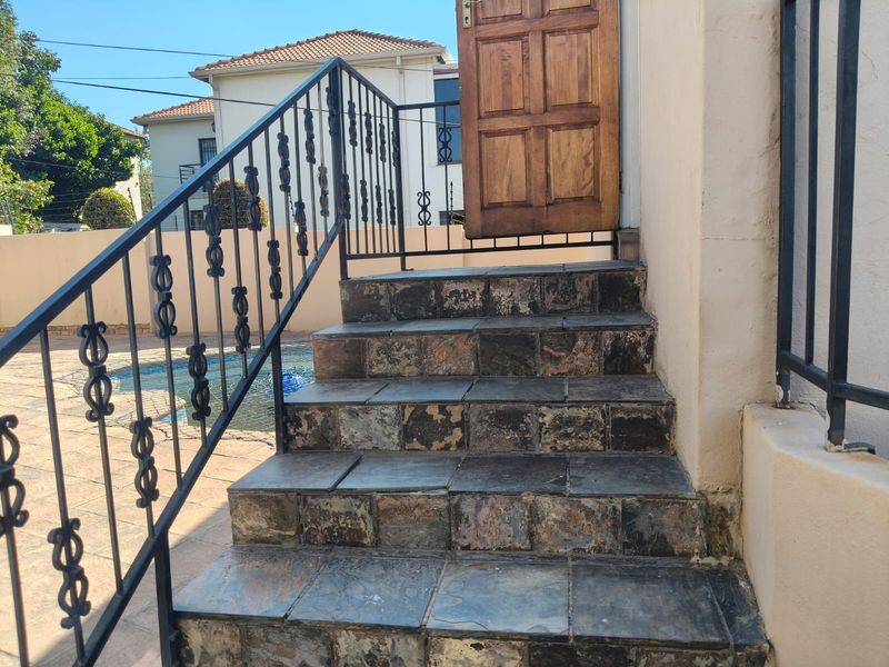 Exterior staircase with wrought iron railings leading to a wooden entrance door, overlooking a pool area.