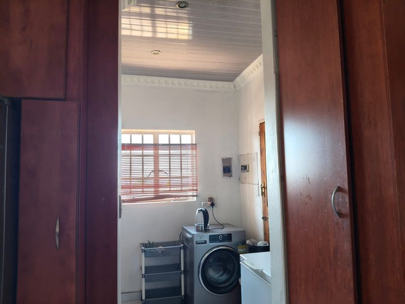 A functional laundry area featuring built-in cabinetry, a timber-look ceiling with recessed lighting, and a window with fitted blinds.