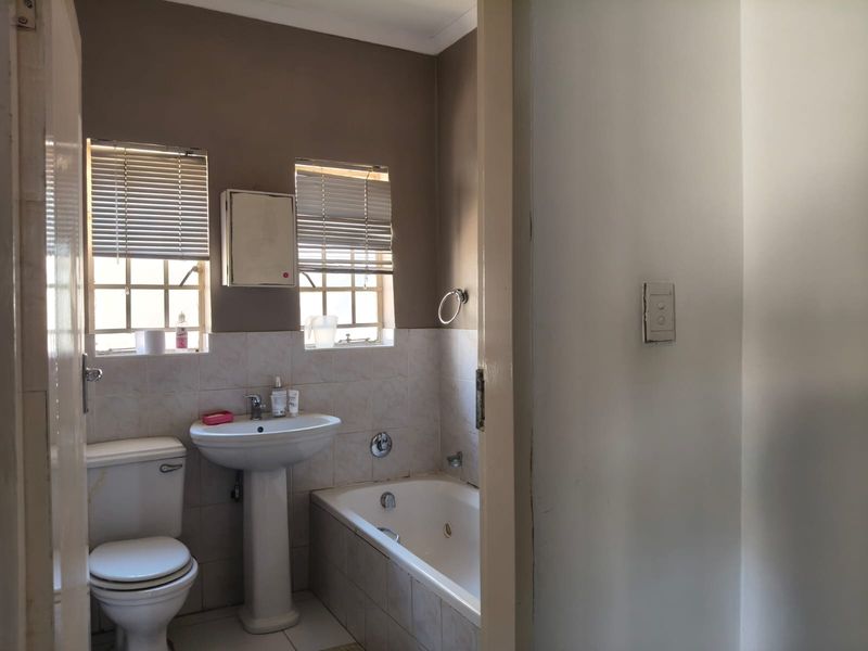 A functional bathroom featuring a pedestal basin, built-in bathtub, and toilet with neutral wall finishes and natural light from dual windows.