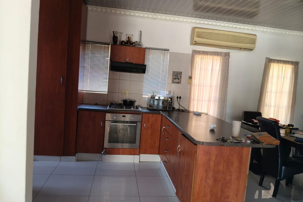Functional kitchen featuring wood-finish cabinetry, built-in oven and hob, tiled flooring, and a breakfast bar counter, with an integrated air conditioning unit.