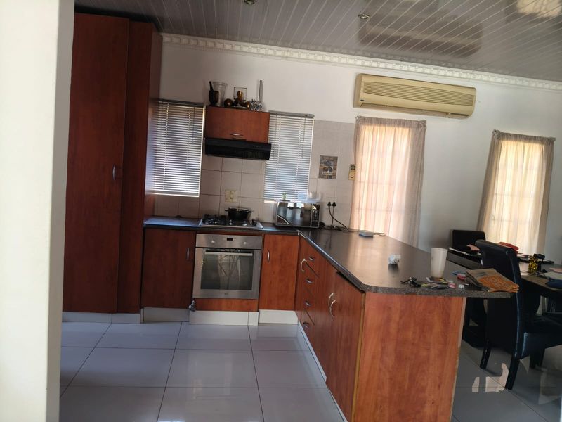 Functional kitchen featuring wood-finish cabinetry, built-in oven and hob, tiled flooring, and a breakfast bar counter, with an integrated air conditioning unit.