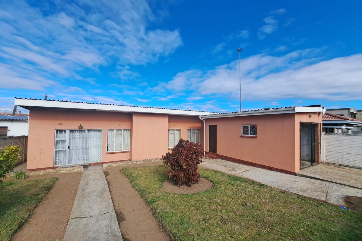 Rear view of a single-story house featuring a concrete walkway, paved driveway, and security gates on the doors and windows.