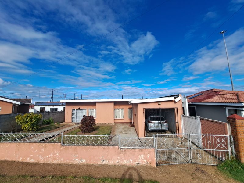Front elevation of a single-story house featuring a concrete driveway, attached garage, and perimeter wall with metal security gate.