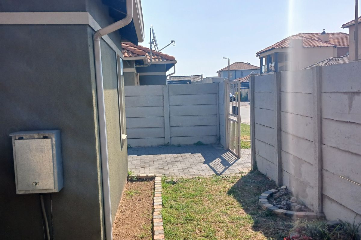 A side yard area featuring a paved walkway, precast concrete boundary walls, and a metal pedestrian gate leading to the street.
