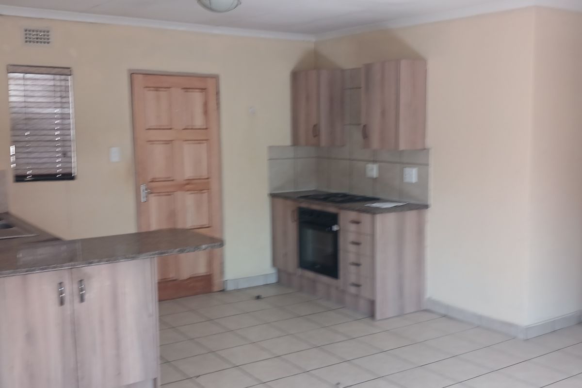 A functional kitchen featuring light wood-toned cabinetry, granite countertops, built-in oven and hob, and tiled flooring throughout.