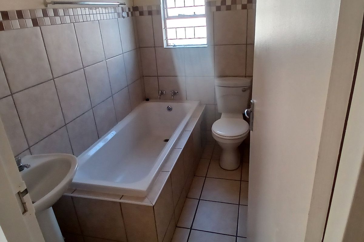 A functional bathroom featuring a bathtub, pedestal basin, and toilet with neutral wall and floor tiling.